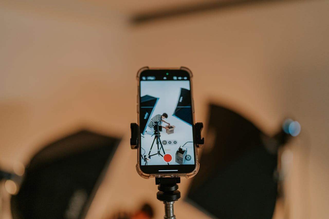 Close-up of a smartphone on a tripod capturing a photo shoot in a studio setting.